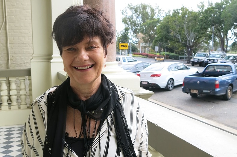 A woman stands on a balcony with a carpark in the background.