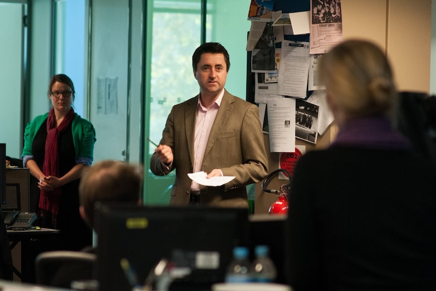 Man standing in newsroom talking to staff.