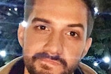 A close up of a young man with a light beard and fashionable hairstyle.