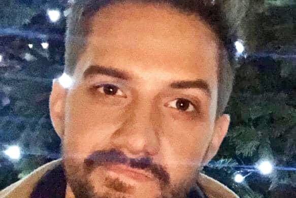 A close up of a young man with a light beard and fashionable hairstyle.