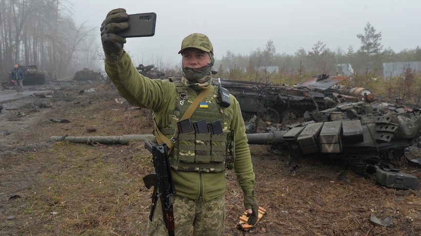 A Ukrainian service member takes a selfie in a front of a destroyed Russian T-72 tank.