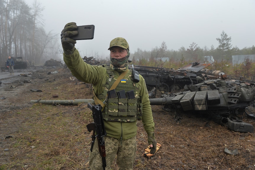 A Ukrainian service member takes a selfie in a front of a destroyed Russian T-72 tank.