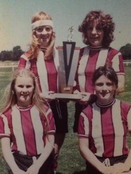 Four soccer players wearing red and white stripes pose for a photo with a trophy