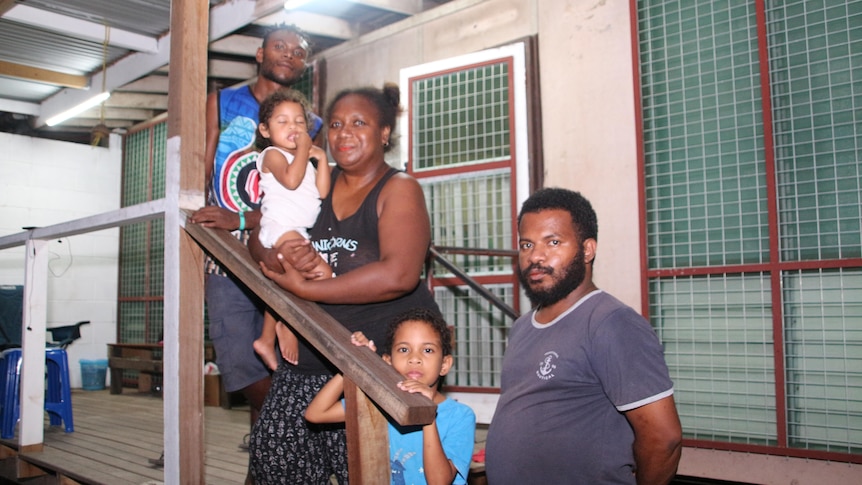 Woman, two children and two men face camera in front of house.
