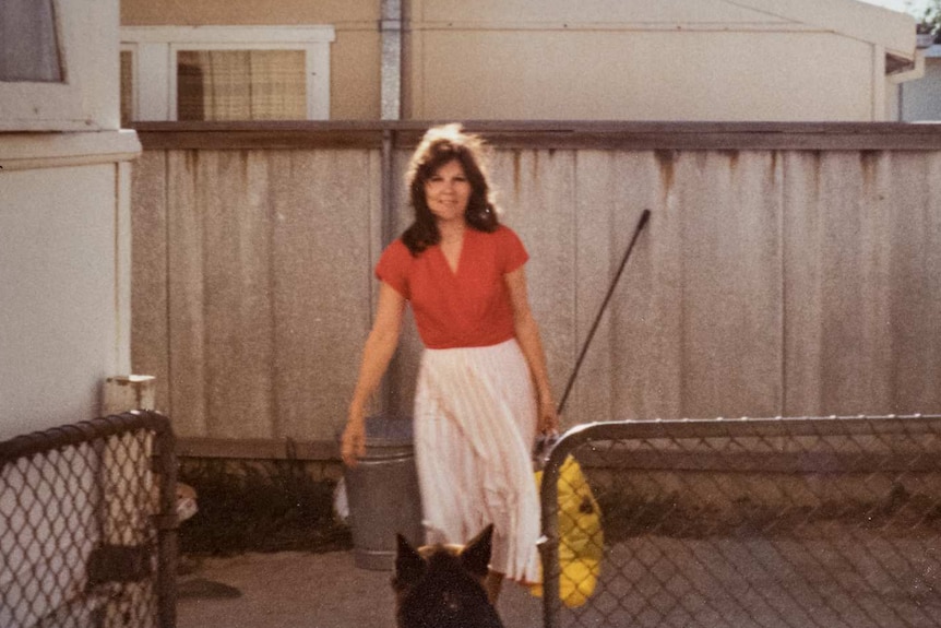 A woman smiles as she carries a bag into a backyard