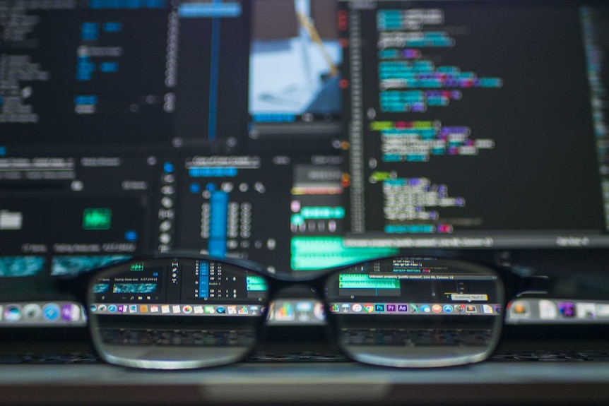 A computer screen with code, and in front of that, a pair of glasses.