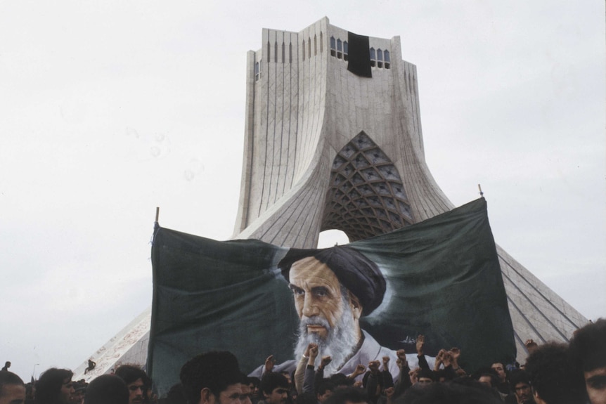Wide archive shot of a large banner with the image of Ruhollah Khomeyni and a crowd in the foreground.