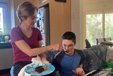 Karen McKenzie sits on the arm of a sofa and feeds her son Jarrod, who has an electric keyboard on his lap