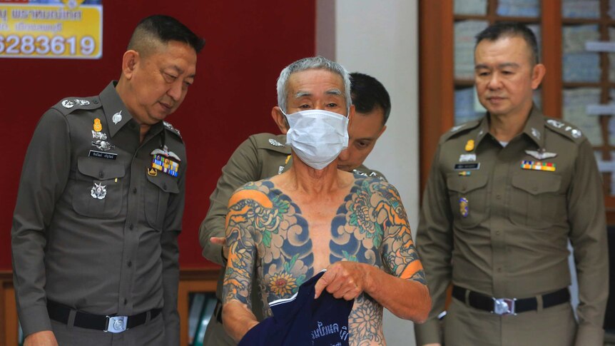 Police inspect a tattoo covering the upper body of a shirtless man.