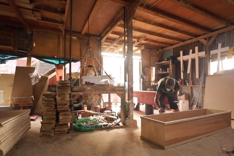 A room where two coffin makers are preparing a plywood coffin. 