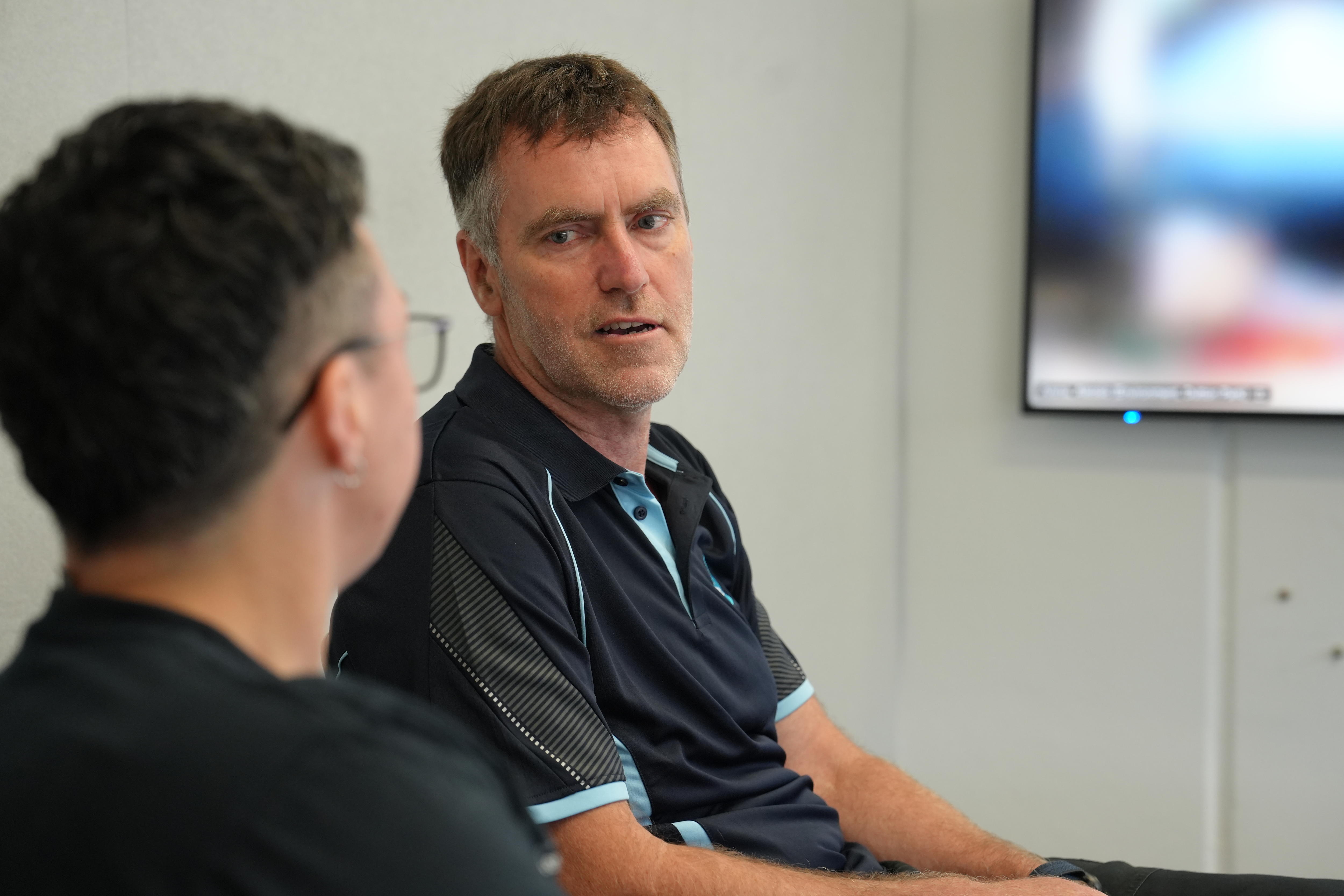 Justin Leonard talks to a colleague in a meeting room.