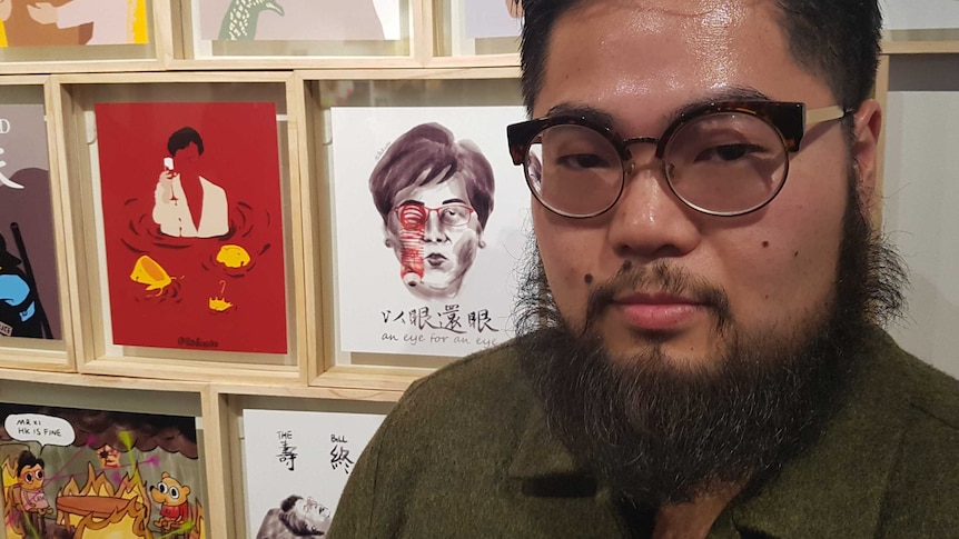 Badiucao stands in front of framed samples of his work