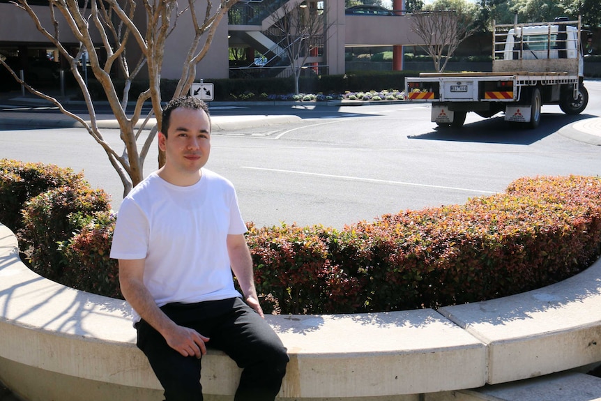 Man sitting on bench by plants and road.