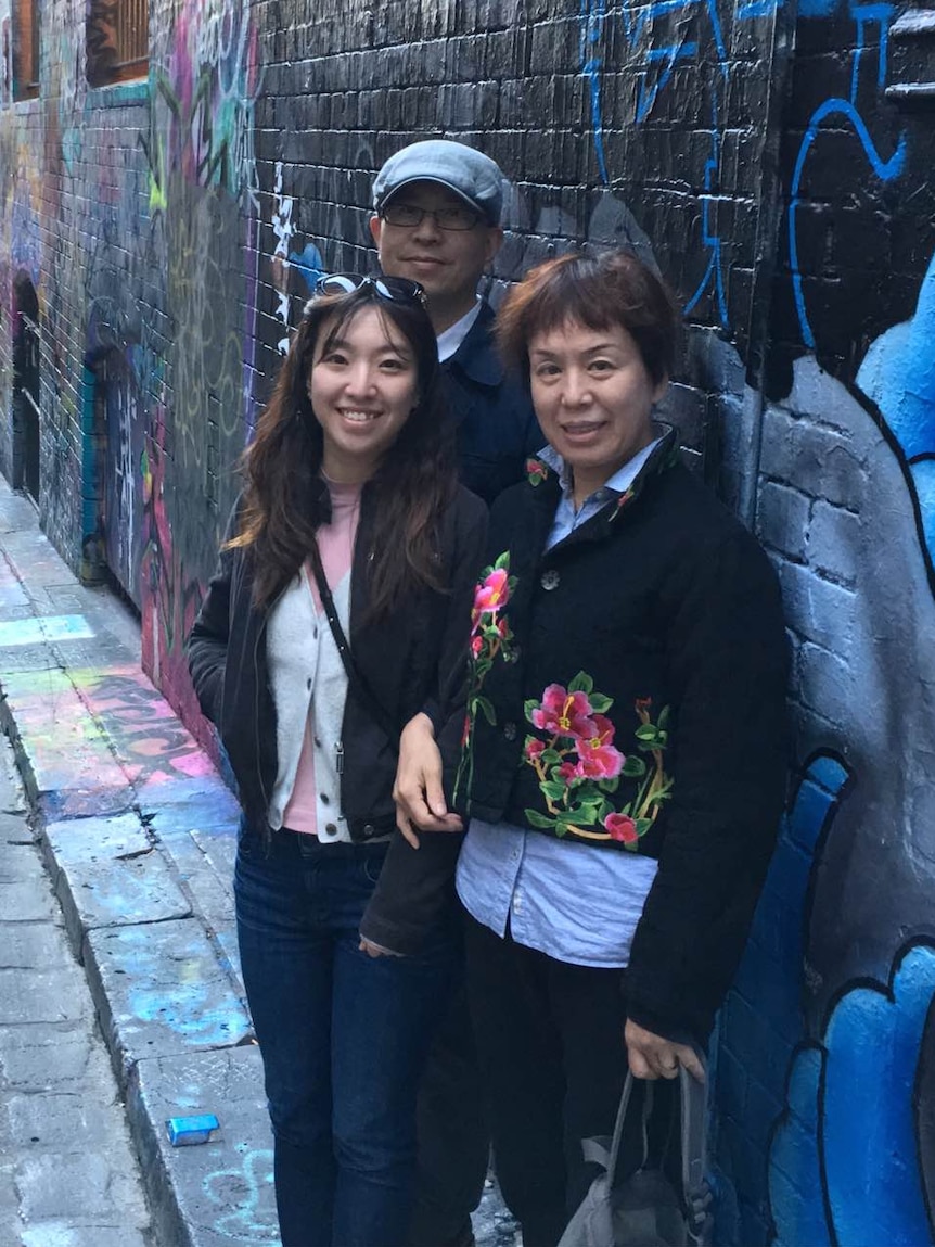 Nicole Xie and her parents standing against a wall decorated with graffiti.