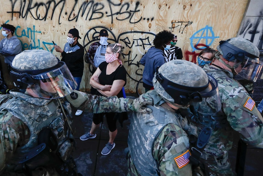 Three army personnel wearing camo move through a crowd of people