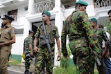 A group of Sri Lankan security forces, some armed with large weapons, stand outside a large white building.
