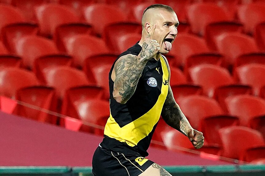 A Richmond AFL player pumps his right fist and sticks his tongue out as he celebrates a goal against West Coast.