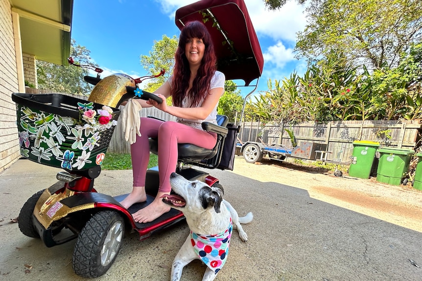 Woman smiling on mobility scooter with black and white dog looking up at her