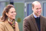 Kate and Prince William smile, not looking directly at the camera. They're both wearing brown coats. 