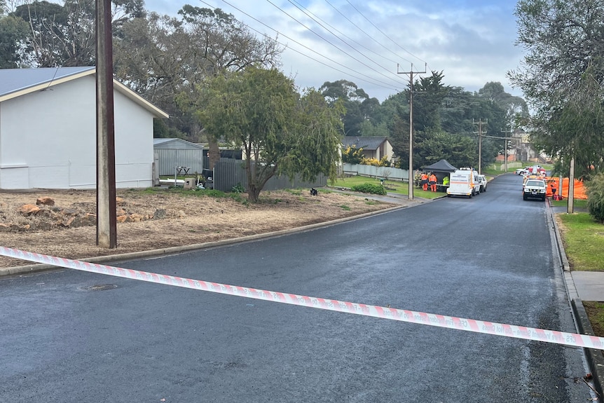 A suburban street with orange and white tape blocking off an area, with emergency services vehicles outside a house