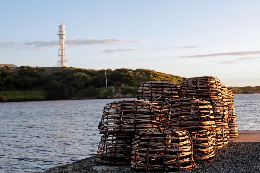 A row of cray pots at sunset on a harbour with water and a lighthouse in the background