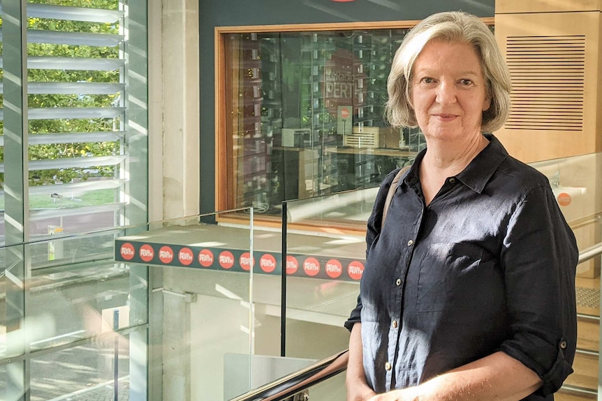 A middle-aged woman with short blonde hair looks at the camera