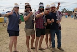 Five young men in sunglasses, shorts and thongs face the camera