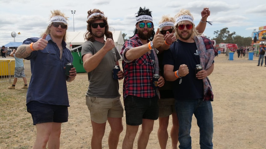 Five young men in sunglasses, shorts and thongs face the camera