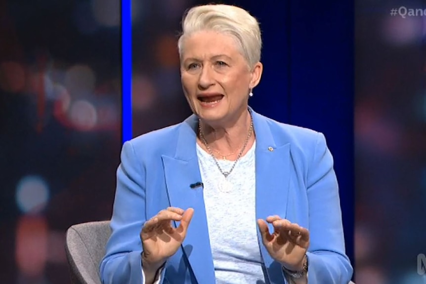 A woman in a light blue blazer and white shirt with short light hair.