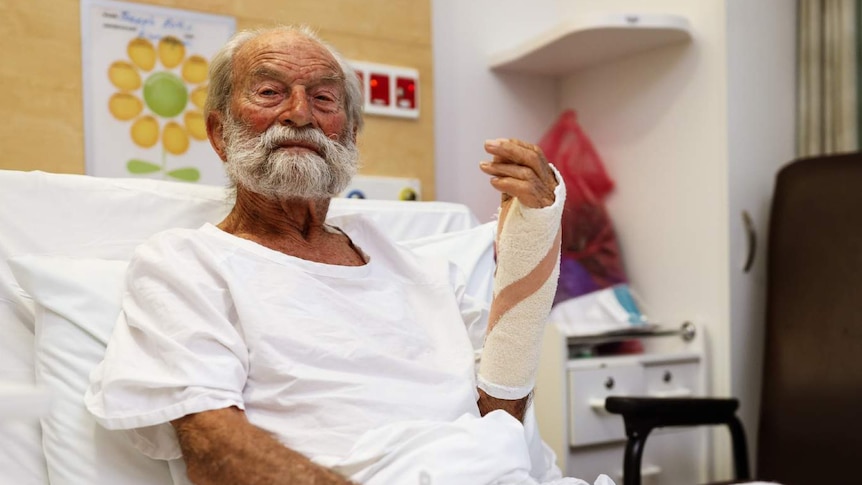 A man sits in a hospital bed with a cast on his arm