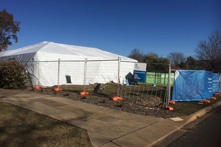 White tent over house and fences around, blue tarp, soil upturned.