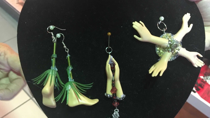 Earrings made out of barbie doll feet and hands on a display case