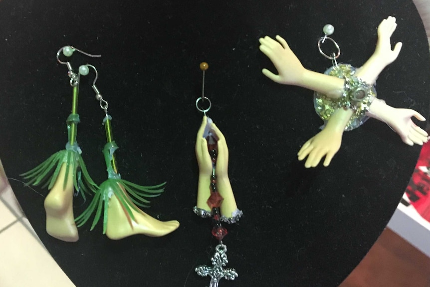 Earrings made out of barbie doll feet and hands on a display case