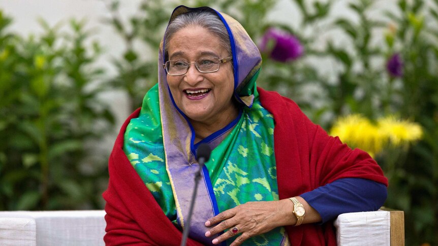 In a brightly-coloured veil, Bangladeshi Prime Minister Sheikh Hasina laughs while leaning against a couch armchair.