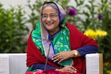In a brightly-coloured veil, Bangladeshi Prime Minister Sheikh Hasina laughs while leaning against a couch armchair.