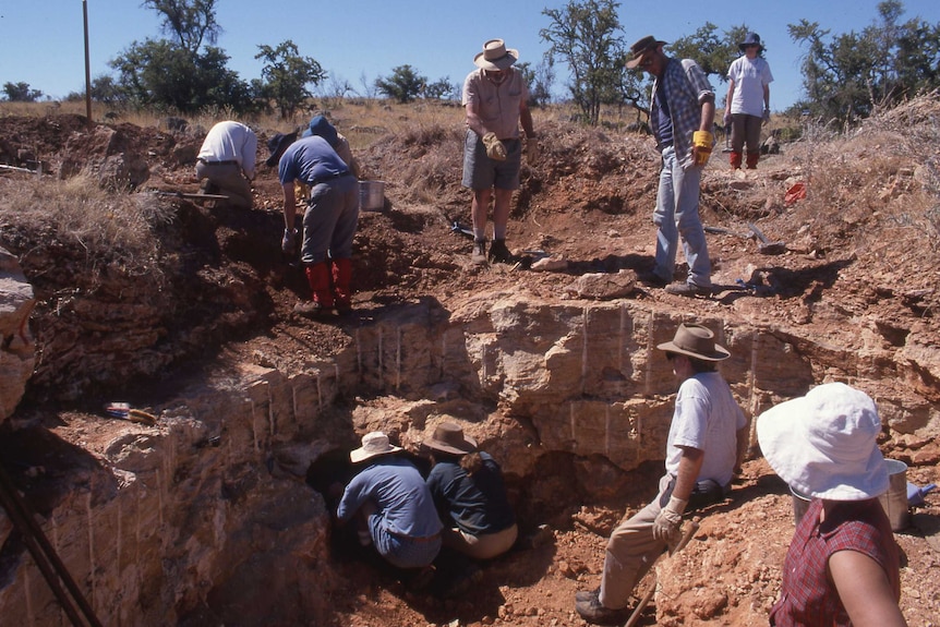 A team of men and women crowd around a large hole in the ground