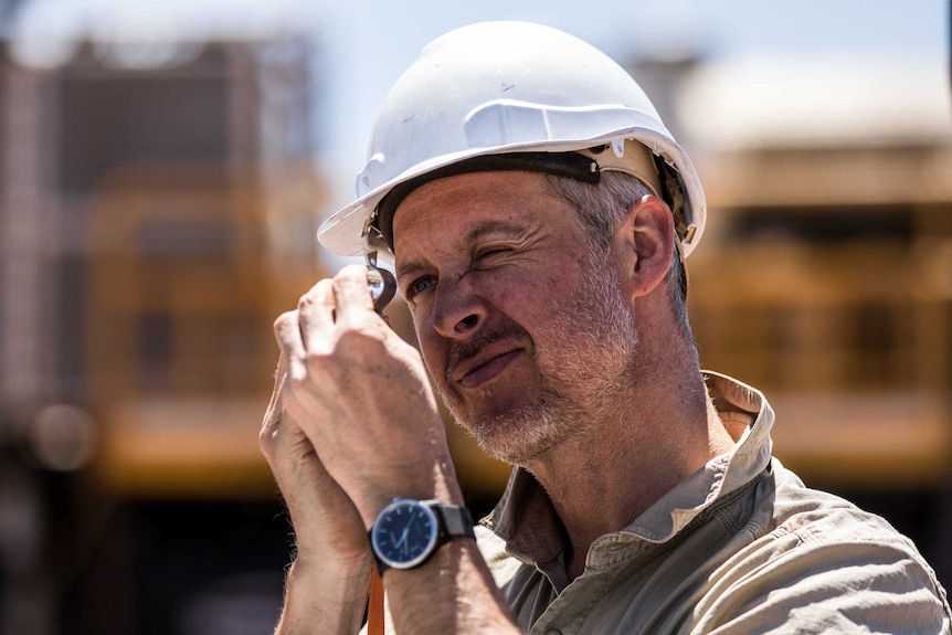 A geologist inspects rock chip samples under a magnifying glass