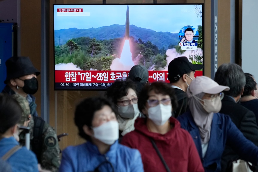 首尔火车站戴口罩的人走在电视屏幕前，电视屏幕显示朝鲜正在发射导弹