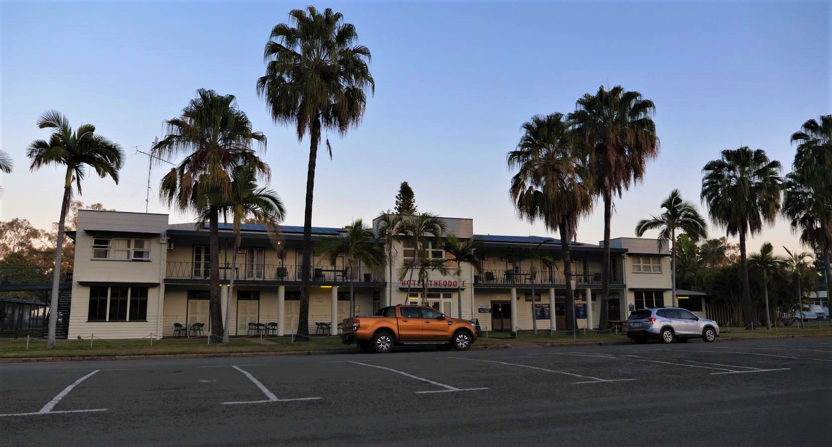A wide shot of the hotel. There's palm trees in front.