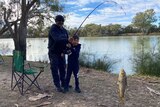 A man and a child hold a fishing rod with a fish on the hook. 