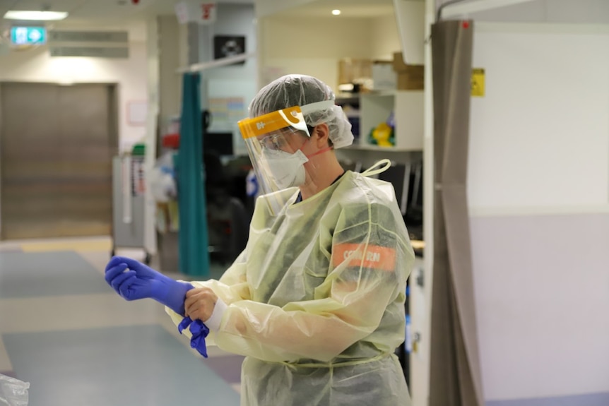 A health worker in full PPE puts on her gloves. 