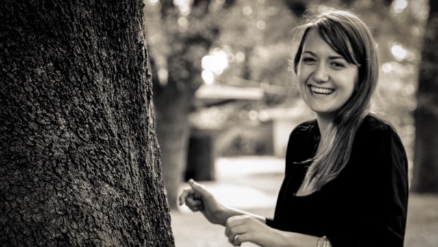 A black-and-white photograph of Courtney Herron, a young woman with light brown hair, smiling in a garden.