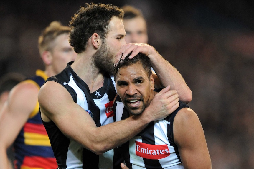 One AFL player hugs another and kisses his head on the football field.