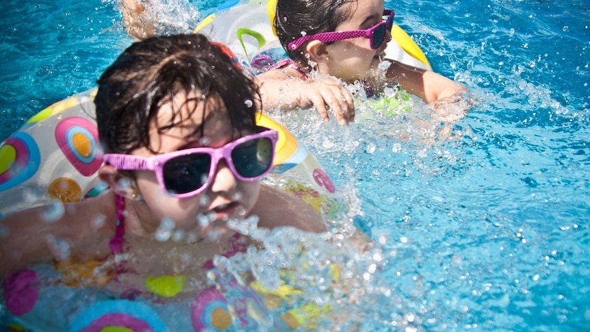 Two girls swimming in pool wearing floaties, wearing pink sunglasses