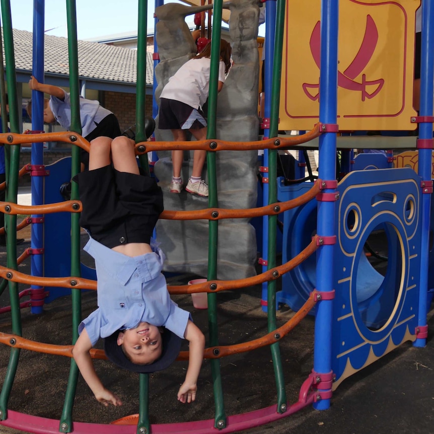 A child hanging upside down on play equipment outside.