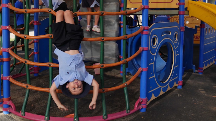 A child hanging upside down on play equipment outside.