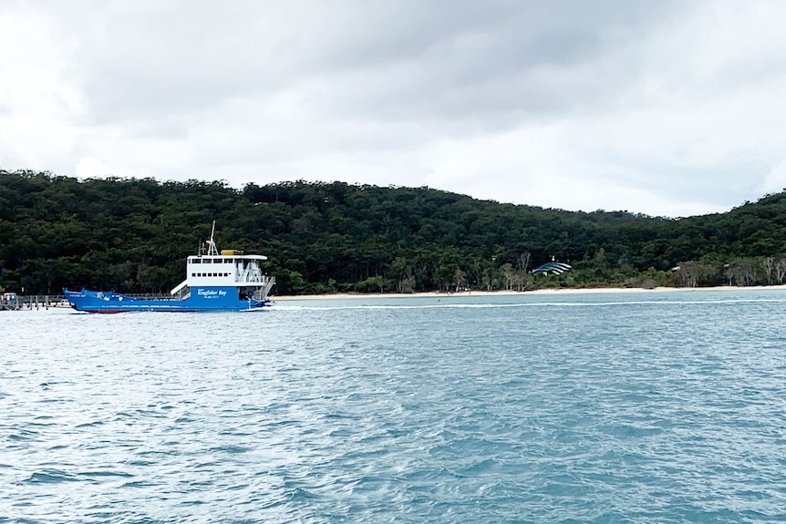 Blue vehicle ferry approaches jetty on Fraser Island, with Kingfisher Bay Resort in bushland in the background.