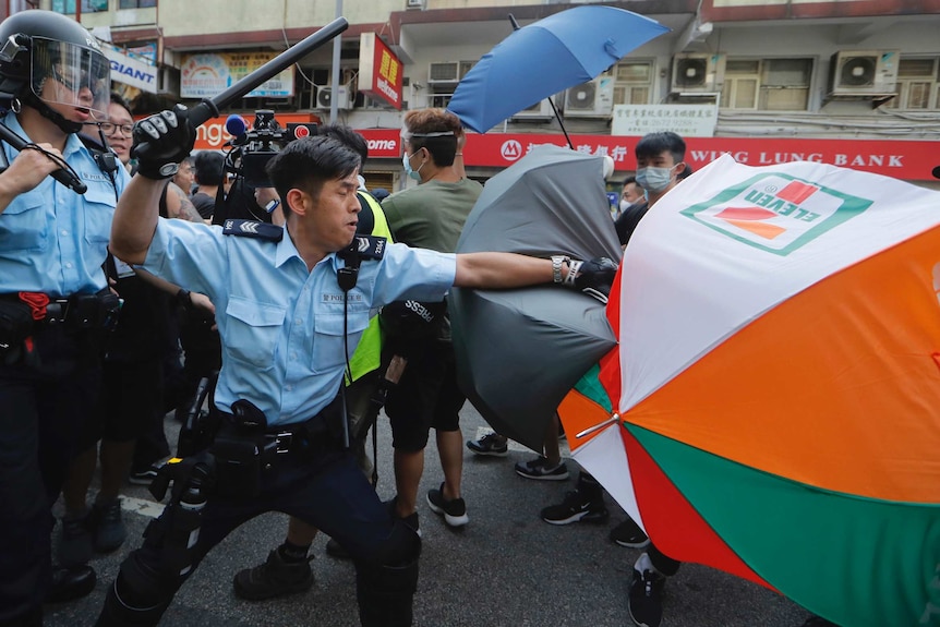 A police officer attacks protesters holding up umbrellas in Hong Kong.