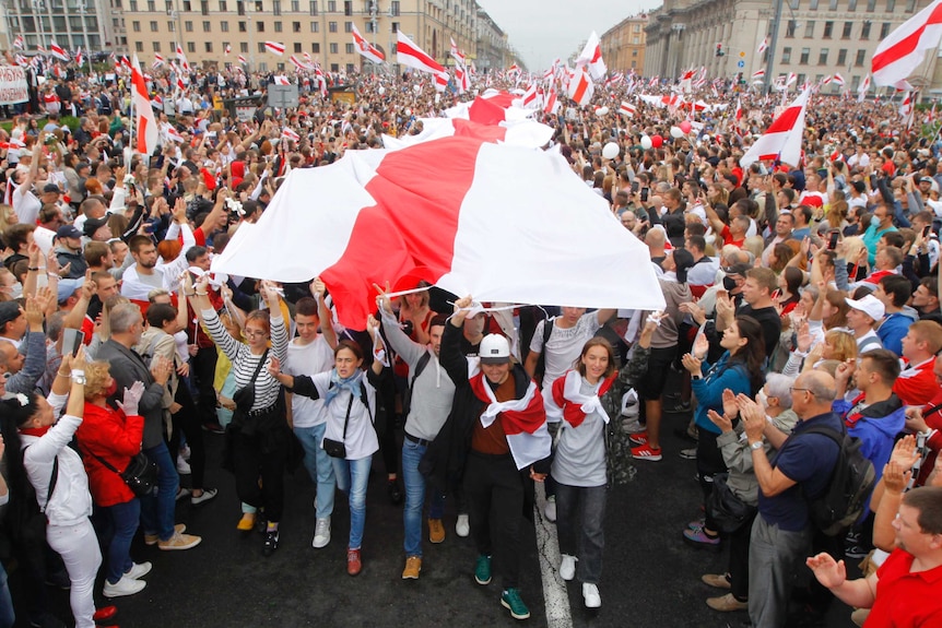 A group of protesters carry a long red and white flag through a cheering crowd of thousands.