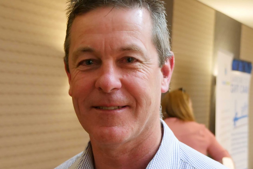 A man, wearing a light blue shirt, smiling.